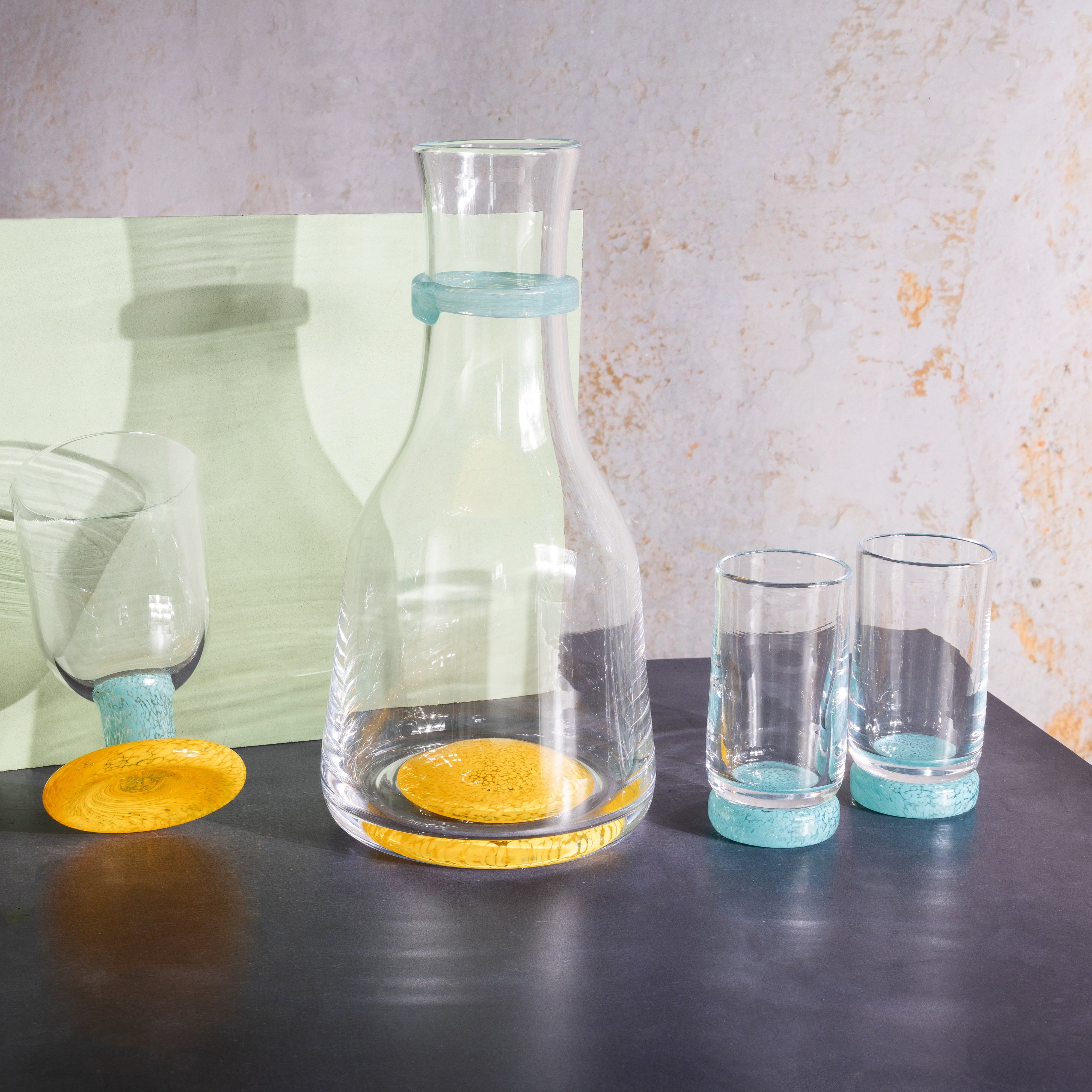 Set of glass carafes and tumblers with yellow and blue accents on a dark surface.