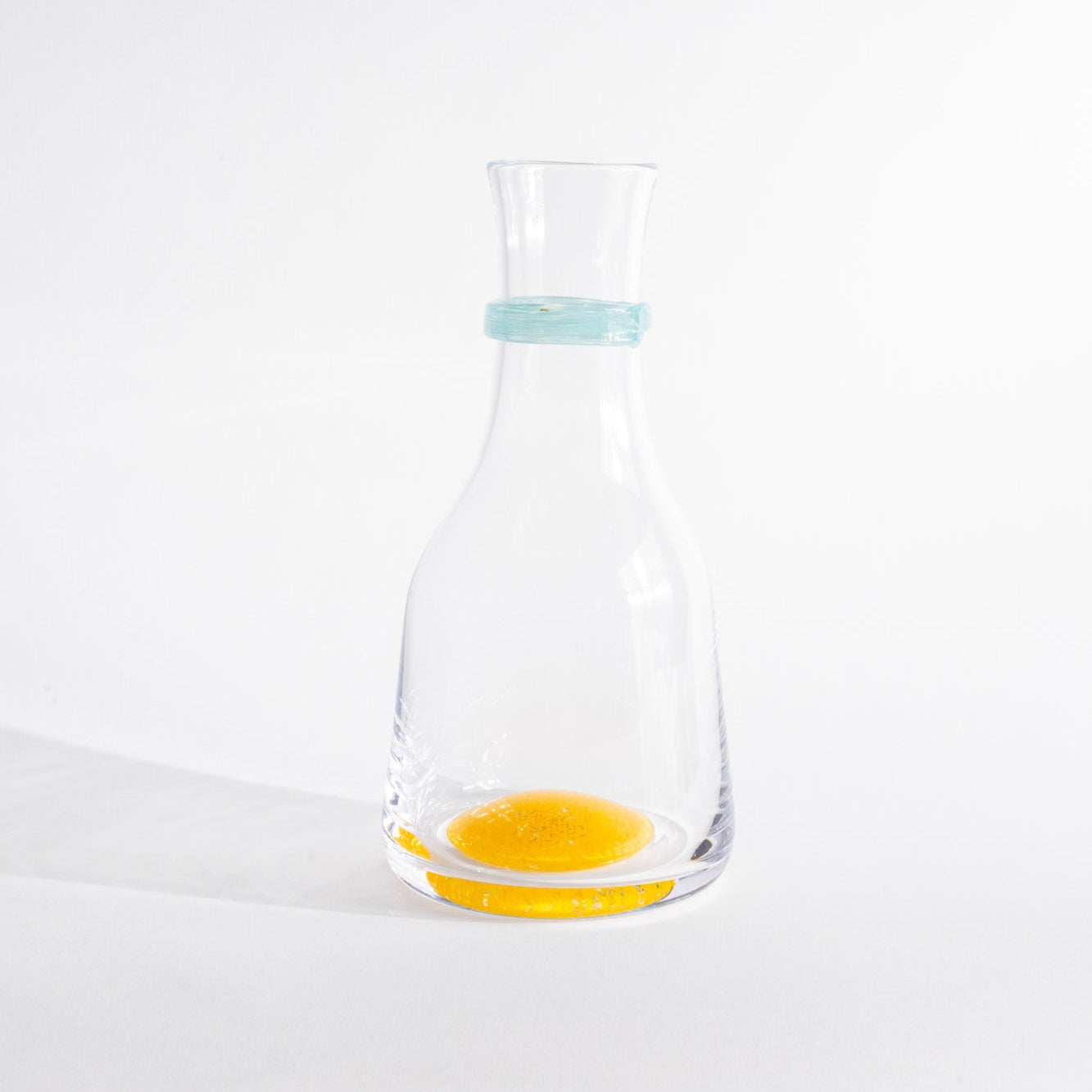 Clear glass carafe with a small amount of yellow liquid on a white background